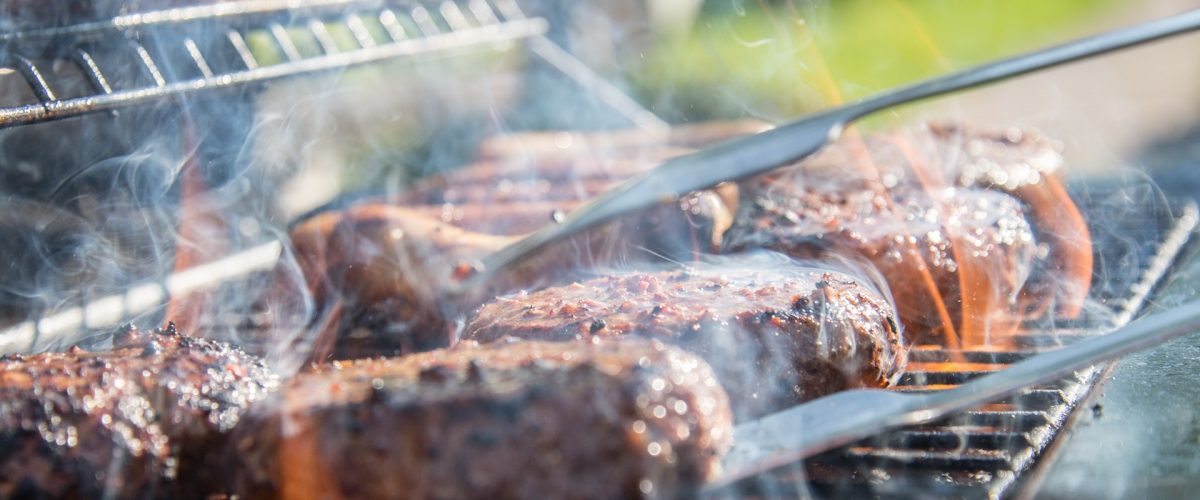 Burgers grilling on a barbeque with a pair of kitchen tongs