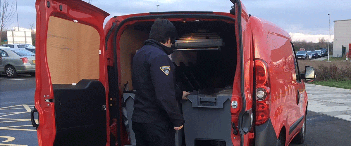 A red van with the back doors open with a member of staff in uniform getting something out of the boot