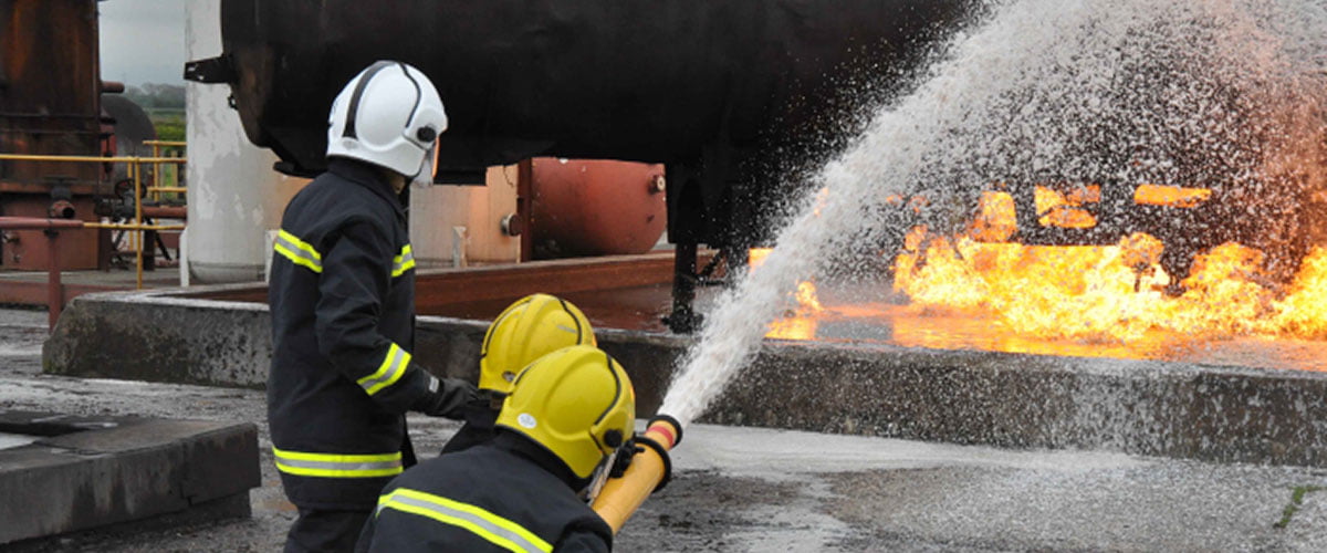 Youngsters squirting a water hose towards a fire in the distance