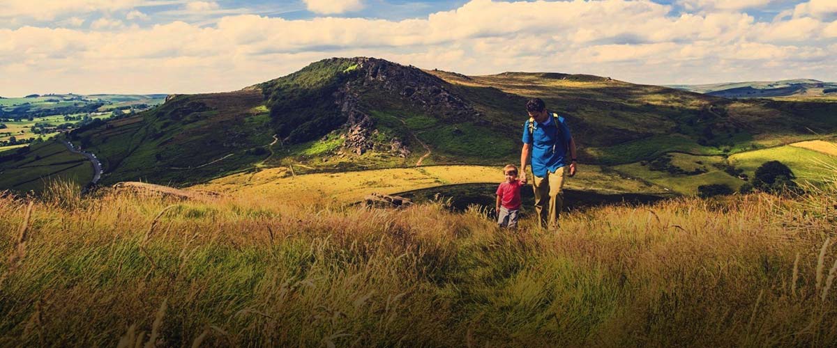 Greenery in the countryside with a parent and toddler holding hands walking