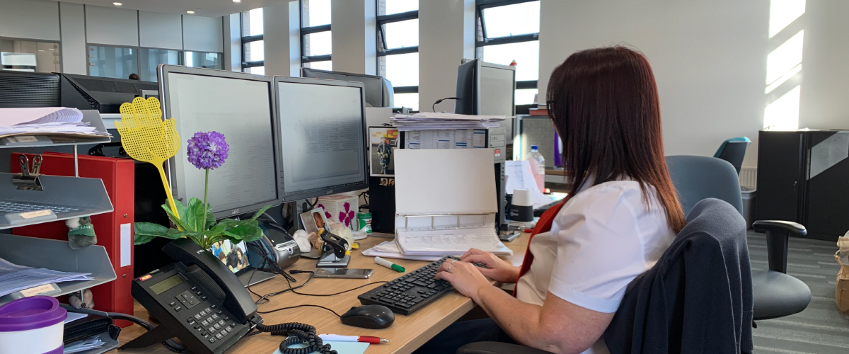 A member of staff in uniform sat infront of a computer at a desk typing