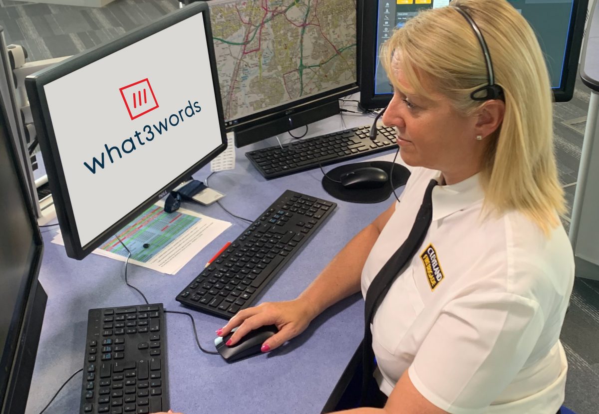 women sat at a desk upright in front of a computer screen with the words what 3 words on the screen