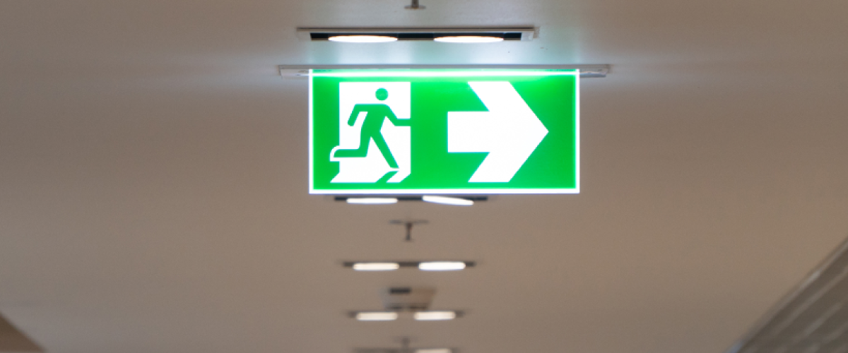 A green fire exit sign hanging from a ceiling