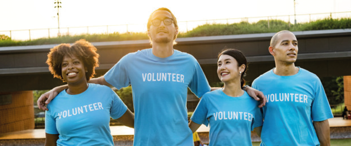 four volunteers smiling together with volunteer printed on their t-shirts