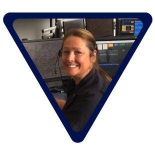 image of a woman smiling facing the camera sat in front of computer screens with a headset