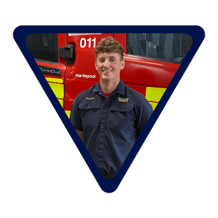 male firefighter stood in front of a fire engine wearing blue uniform