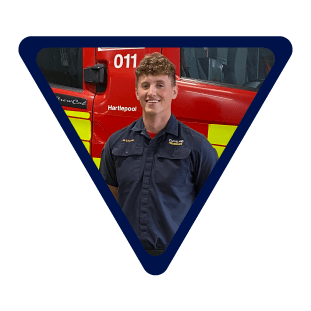 male firefighter stood in front of a fire engine wearing blue uniform