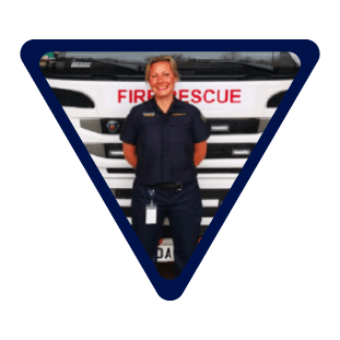 female firefighter stood in front of a fire engine wearing blue uniform