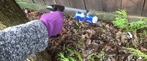 a hand with a litter picker picking up a large drink can