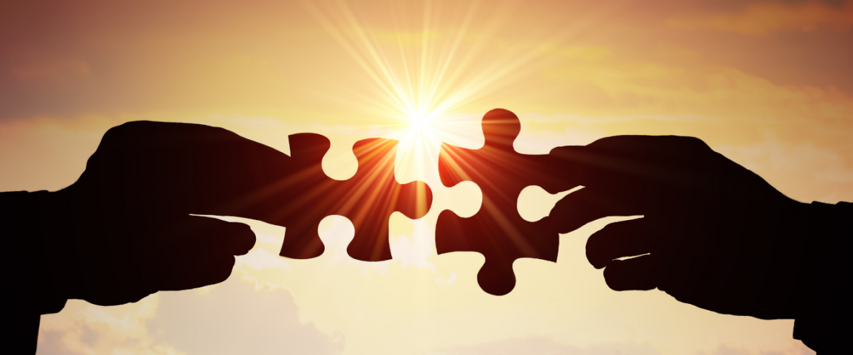 two hands with two pieces of jigsaw joining together with the sun shining though the middle