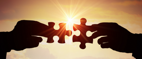 two hands with two pieces of jigsaw joining together with the sun shining though the middle