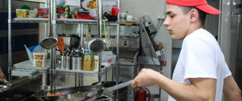 A cook at a takeaway kitchen flipping a pan of food