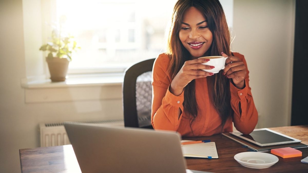 women sat at a desk at home with a coffee in her hand
