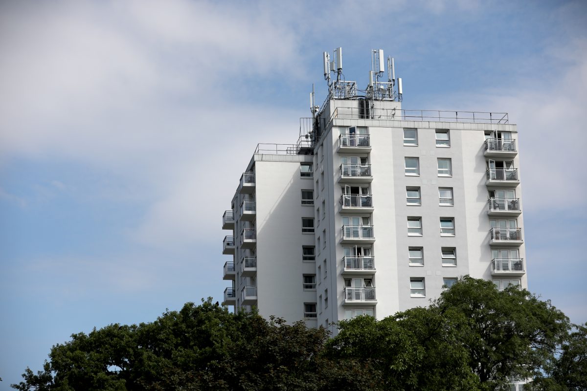 An image of a block of white flats with trees covering the bottom. Blue skies with clouds.