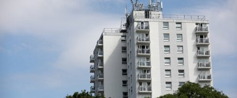 An image of a block of white flats with trees covering the bottom. Blue skies with clouds.