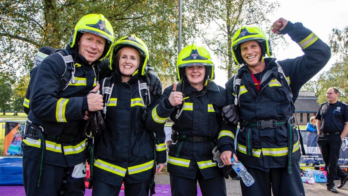Four firefighters at a challenge event in uniform giving the thumbs up