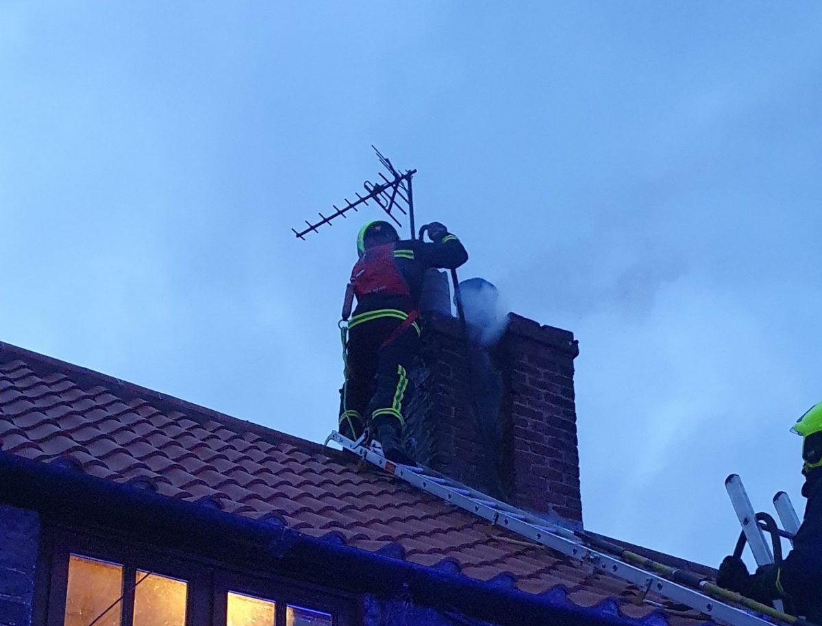 Firefighters on a roof of a house inspecting a chimney