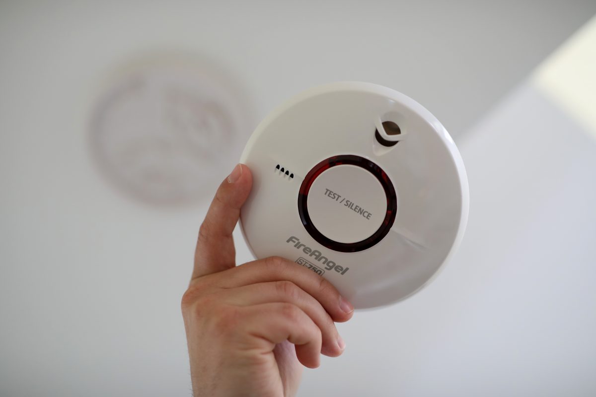 A hand holding a fire angel smoke alarm with a white background
