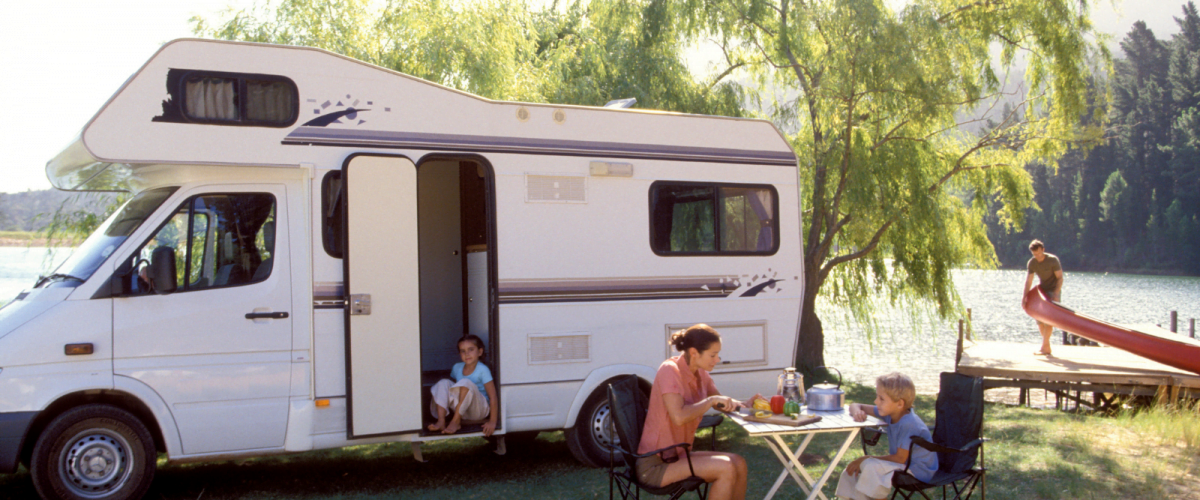 Family caravanning in an open space next to a lake. Sat together on a table outside.