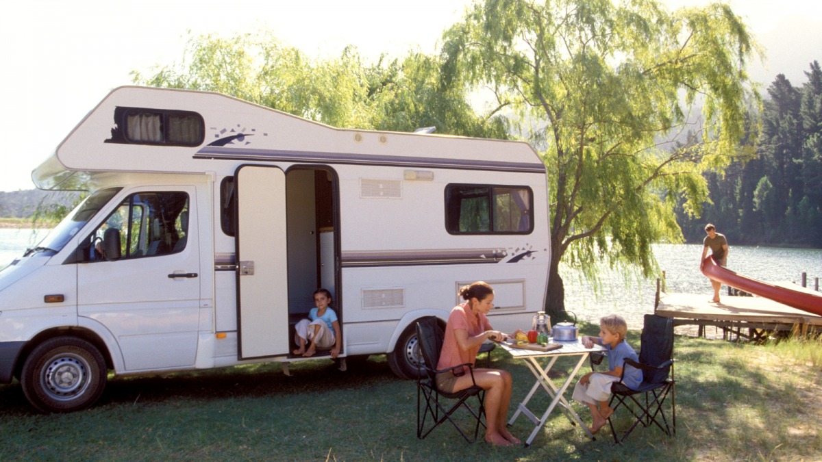 Family caravanning in an open space next to a lake. Sat together on a table outside.