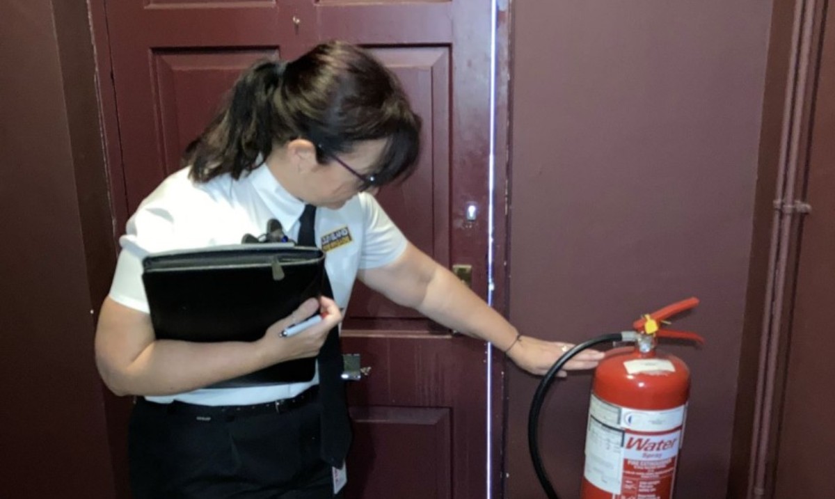 A woman with a clipboard in uniform checking a fire extinguisher