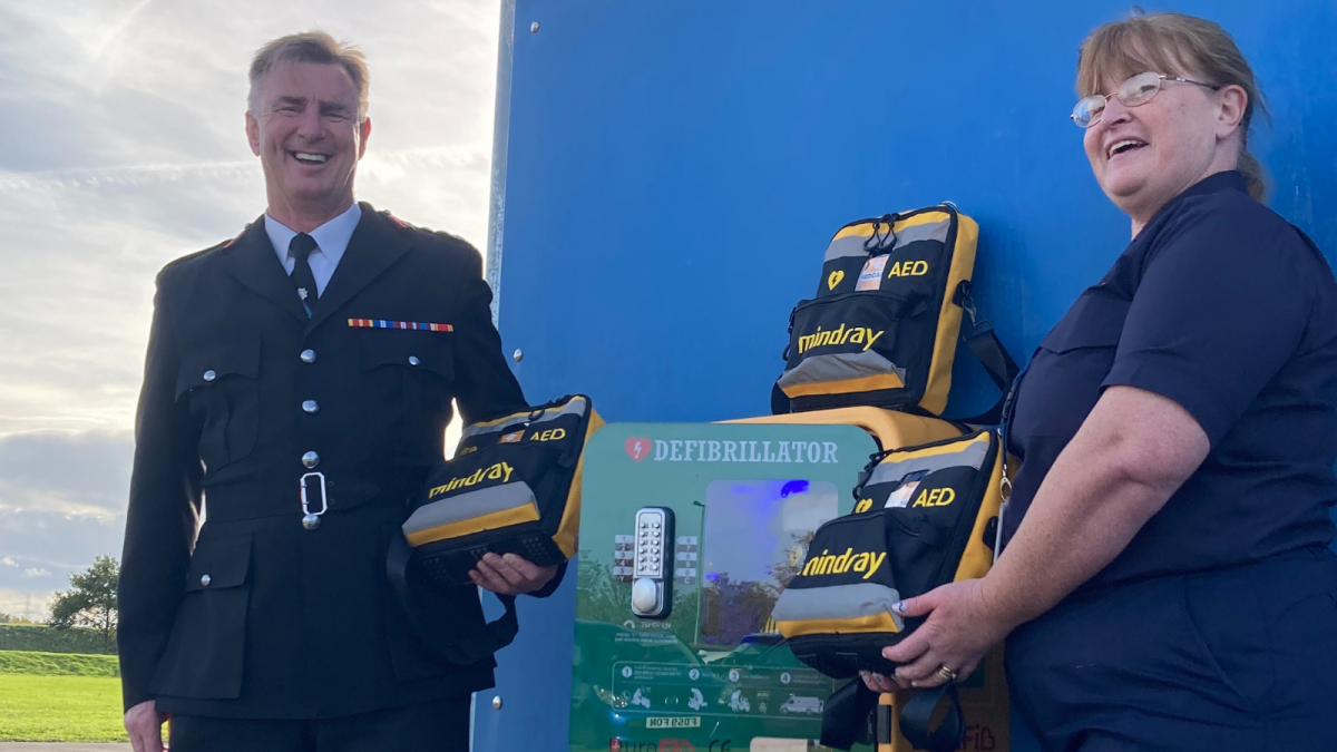 A picture showing our Chief Fire Officer and his colleague stood in between a defibrillator