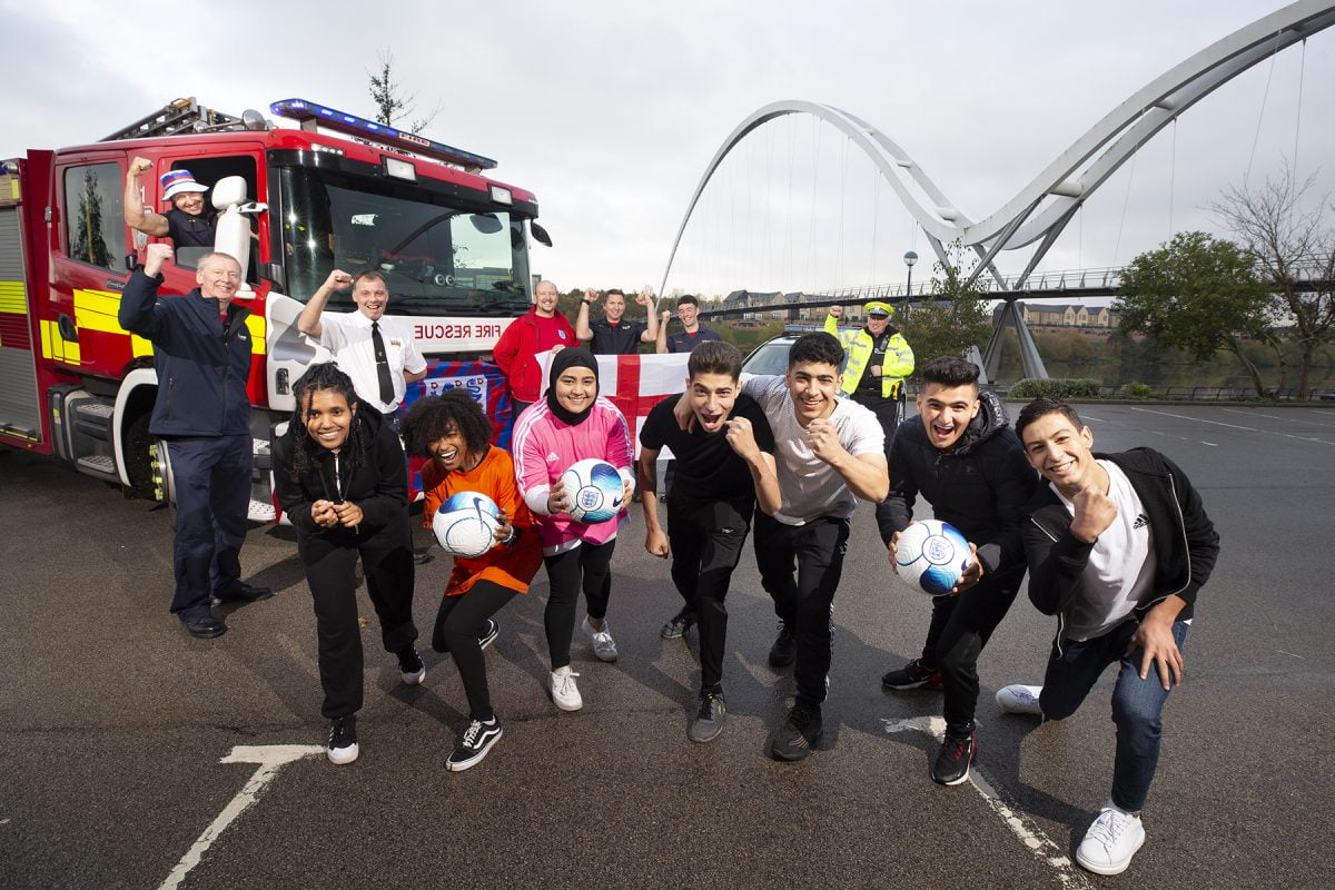 A group of children holding a football alongside a fire engine and police officers