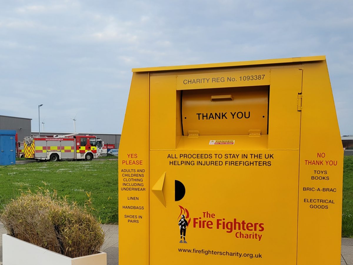 An image of a big yellow clothing bank outside in the distance you can see a fire engine