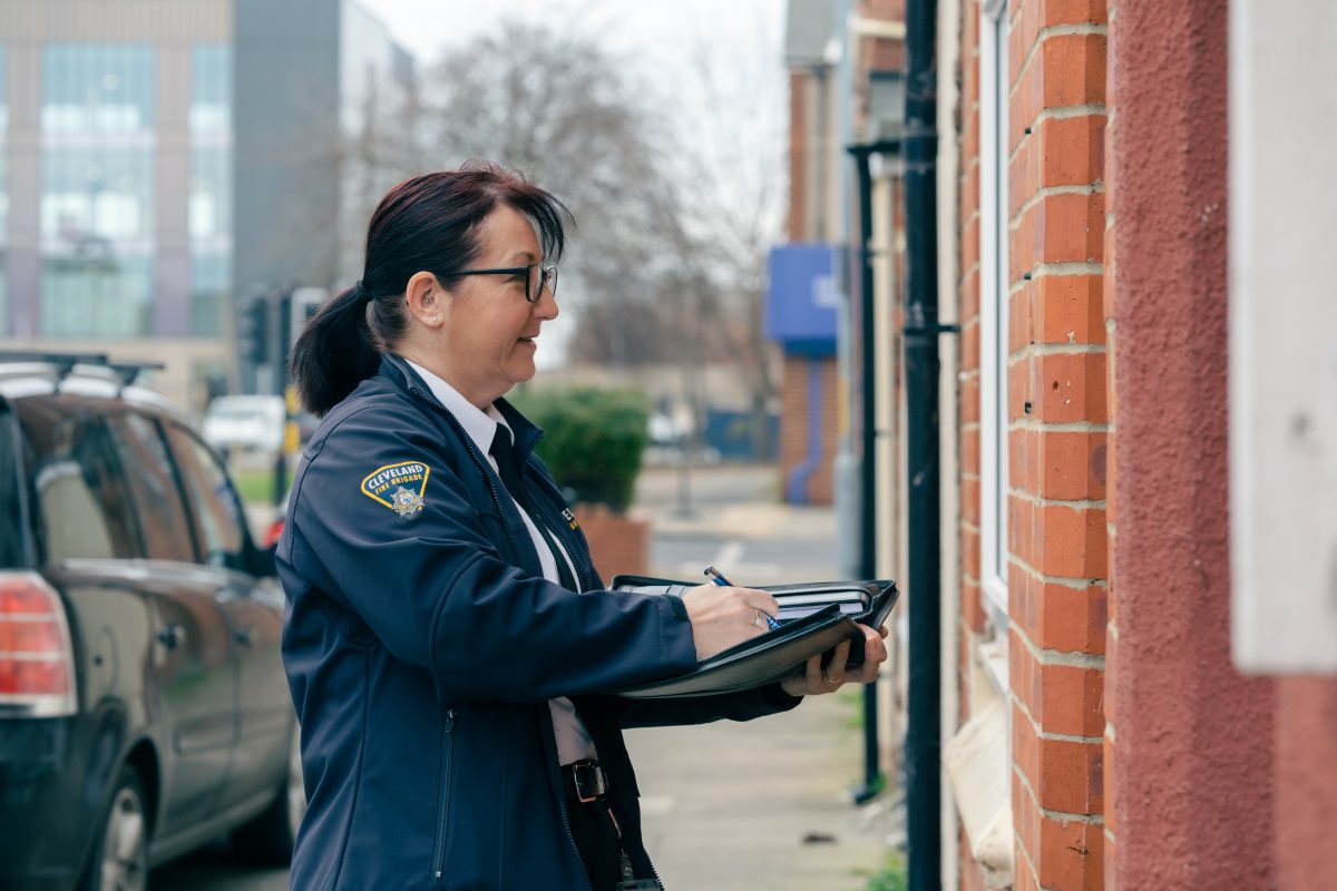 A female member of the fire engineering team holding fire safety documents and standing outside of a building.