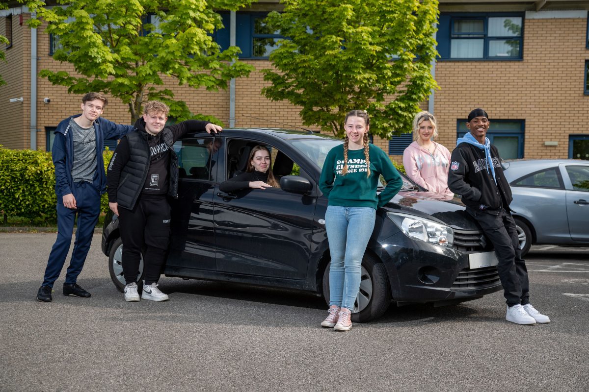 A group of young people stood next to a black car