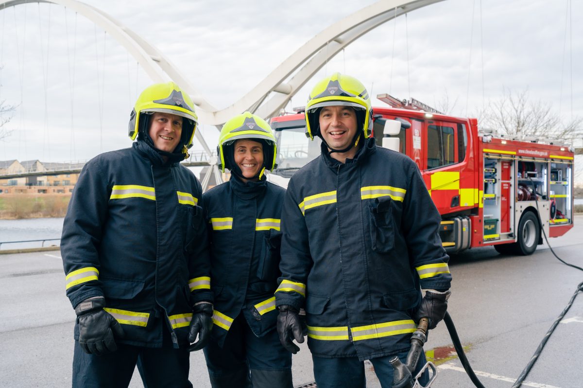 A photo of three firefighter in blue kit stood in front of our fire engine