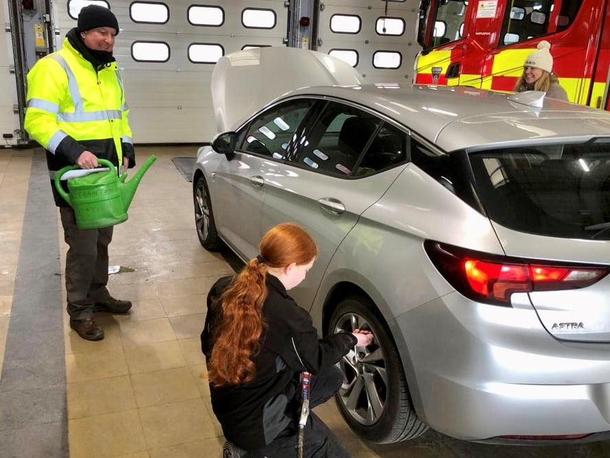 A girl with red hair checking the tyres of a silver car