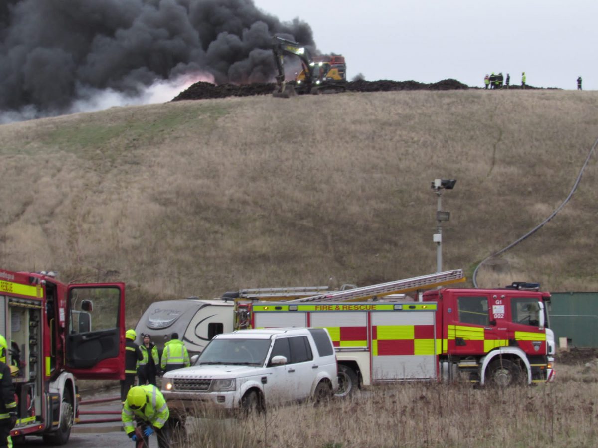 A fire with black smoke and firefighters and fire engines in attendance