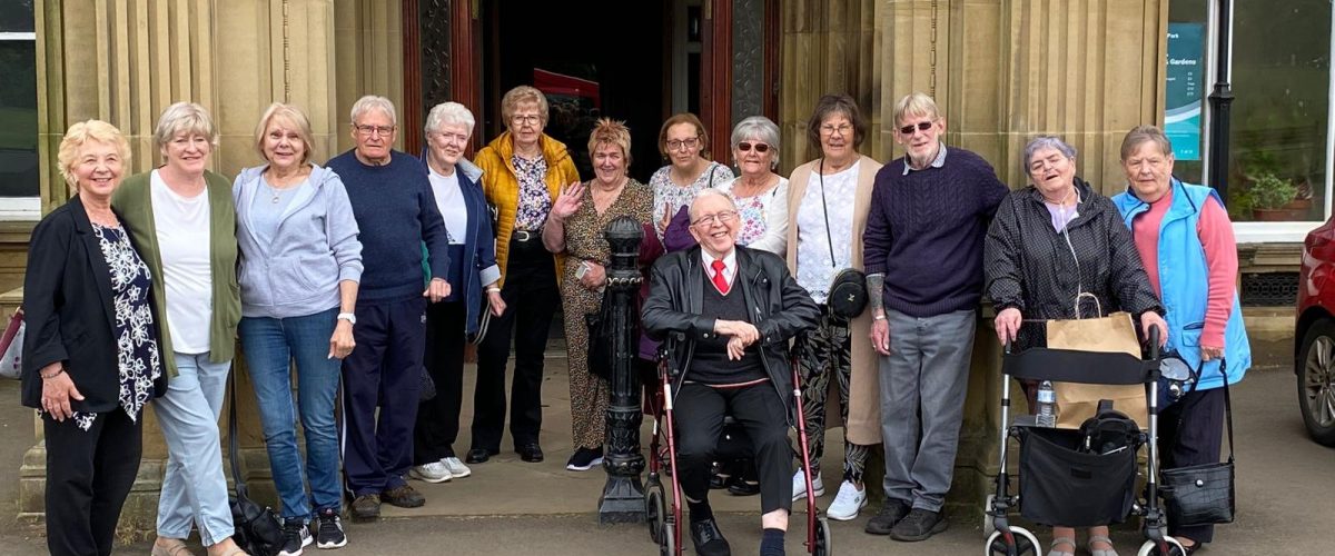 A group of older people stood up or sat down outside of local landmark