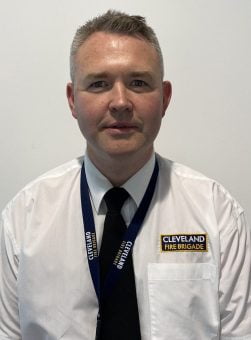A portrait headshot of Peter Rickard (CFO) smiling wearing white shirt, black tie and a lanyard
