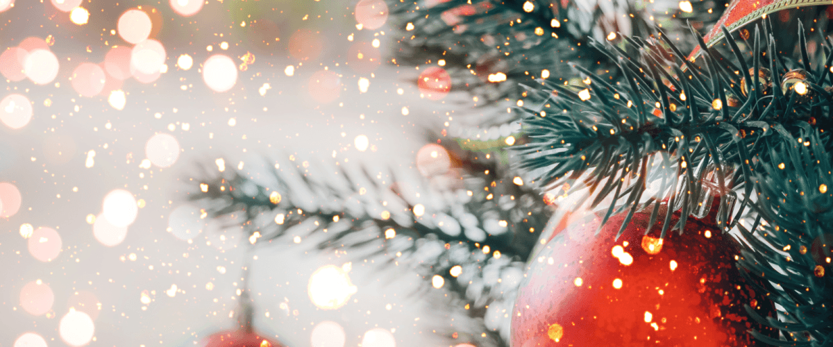 A zoomed in picture of a chirstmas tree with decorations. Fairy light effect over the top and red baubles.