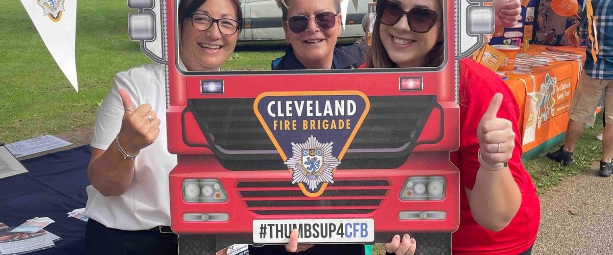 Three volunteers at Middlesbrough Mela stood behind a selfie cardboard cutout of a fire engine