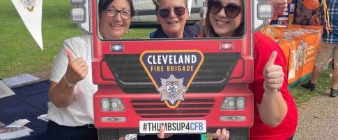 Three volunteers at Middlesbrough Mela stood behind a selfie cardboard cutout of a fire engine