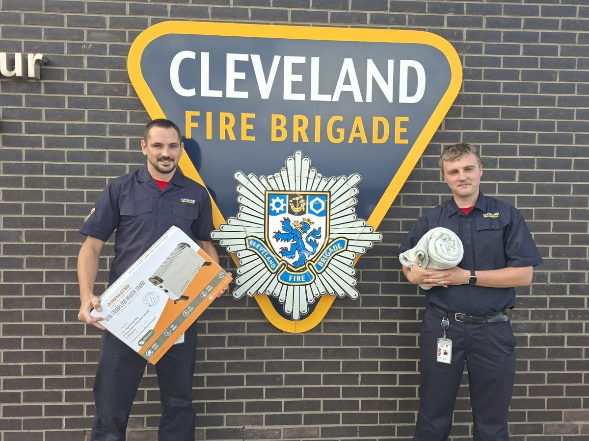 Two members of staff one with a heater and the other with a blanket in front of a cleveland fire brigade logo.