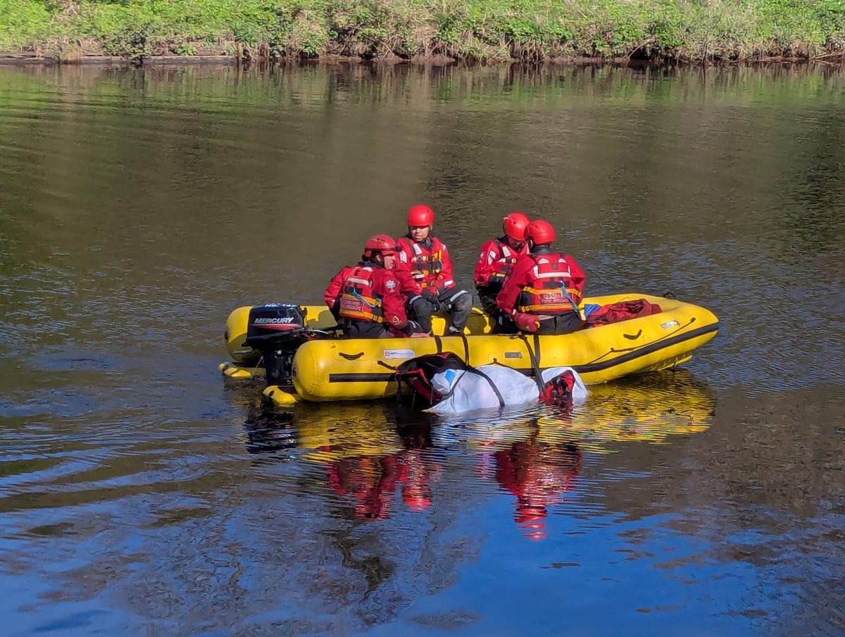 A picture of a lake with a yellow safety boat in the middle, which has four people from Cleveland Fire Brigade on, taking part in water safety trraining