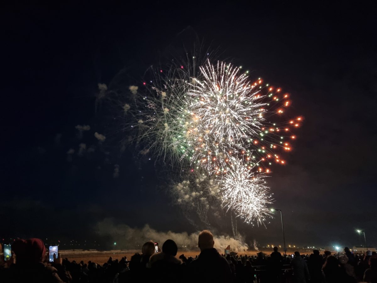 A colourful fireworks display with a large crowd observing